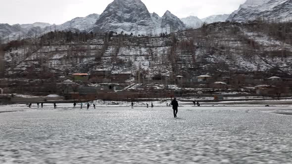 Adult Male Walking Across Frozen Khalti Lake With People Ice Skating In Background . Aerial Low Flyi