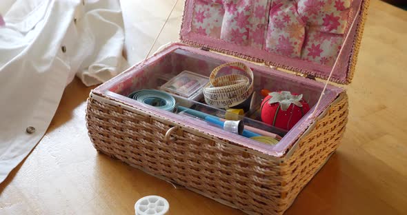 Close up on the hands of an old woman seamstress and her sewing kit as she prepares a white dress sh