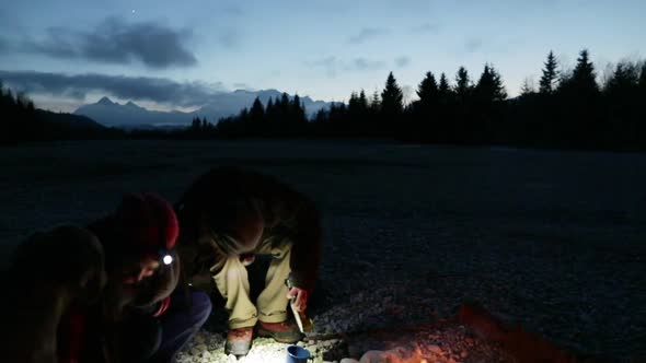 Young man sitting at a bonfire, couple with headlamps sitting down