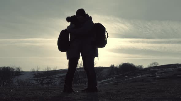 Silhouettes of Two Hikers with Backpacks Enjoying Sunset View From Top of a Mountain