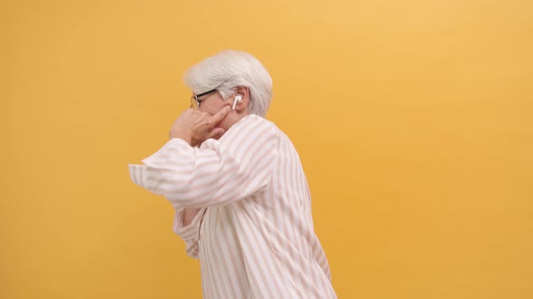 Funny Happy Old Woman Dancing with Wireless Headphones, Isolated on Orange Background