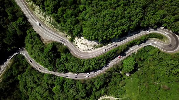 Aerial Fly Over a Curved Winding Road Trough the Mountains with Cars and Truck