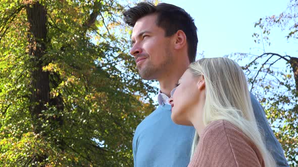 A Young Attractive Couple Looks Into Distance in a Park on a Sunny Day - Closeup From Below