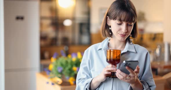 Woman with Drink and Phone in the Kitchen at Home