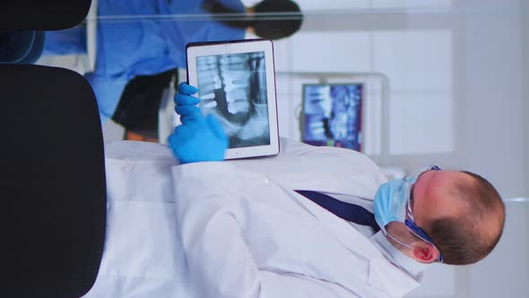 Woman Sitting on Chair Listening Doctor Looking on Tablet with Xray