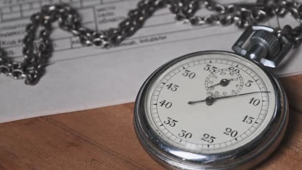 Vintage Stopwatch Lies on Wooden Desk with Old Documents and Counts Seconds