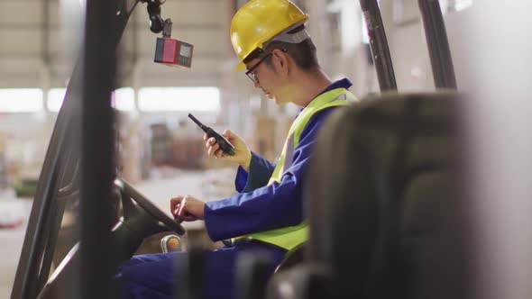 Asian male worker wearing safety suit with helmet talking in warehouse