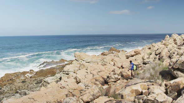 African american man with bag pack walking on the rocks while hiking