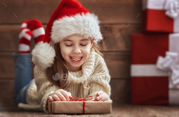 ittle girl with christmas presents on wooden background. Portrait of beautiful child in Santa hat with gifts.