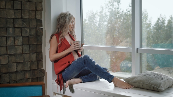 Young Pregnant Woman in Red Shirt Sitting on the Windowsill with the Cup of Tea