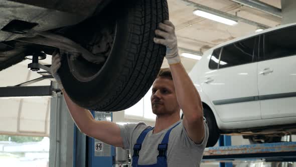 Car Mechanic Examining Car Suspension of Lifted Automobile at Repair Service Station Man