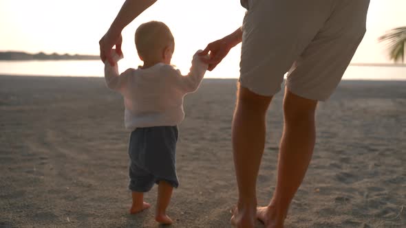 Crop Caucasian Father Teaches a Young Child to Walk on the Sand