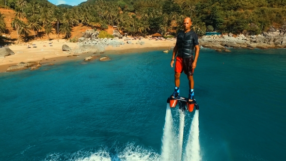 Aerial: Man Standing Over the Water on Flyboard Near the Beach 