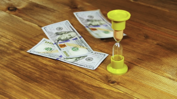 Dollar Banknotes Falling on a Wooden Table and Hourglass