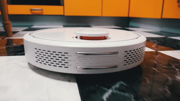 The Robot Vacuum Cleaner Cleans in the Modern House on the Tiles Floor at Kitchen