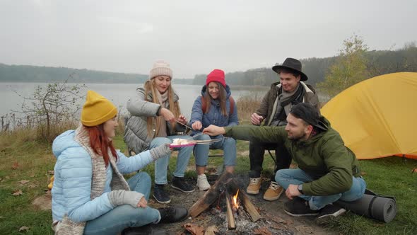 Group of Happy Friends Around Burning Camping Bonfire in Woods Roasting Marshmallows Talking