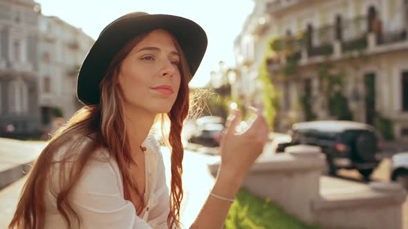 Young Beautiful Girl in Hat Sitting in City Park and Smiling