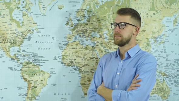 a Young Bearded Man in Glasses Looks at the World Map and Making Plans
