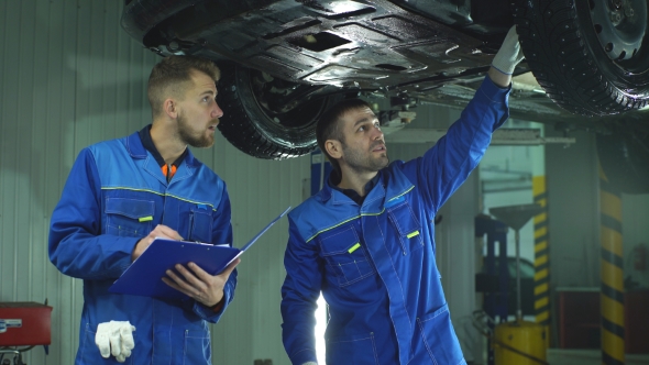 Young Workshop Employees Working Together Underneath a Lifted Car