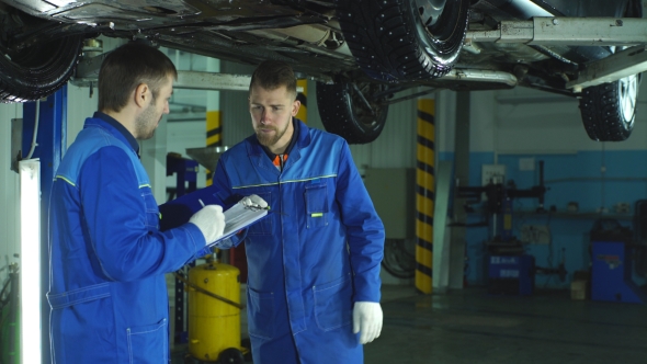 Two Mechanic Checking on a Car Engine and Taking Notes