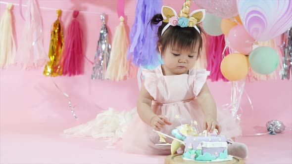 Cute Toddler Eating and Playing with Birthday Cake in Pink Background with Balloons and Decorations