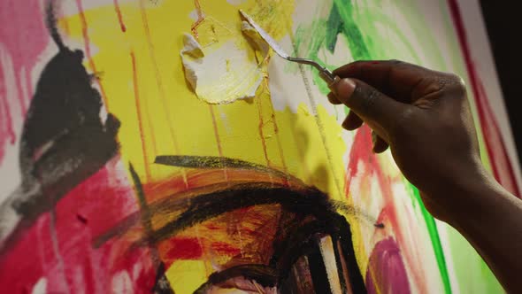 Close up of hand of male artist painting with palette knife on canvas at art studio