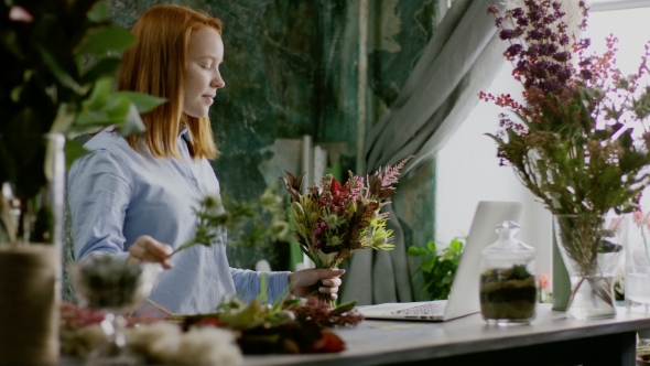 Smiling Florist Arranging Bunch of Flowers Near Computer