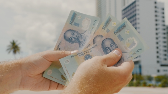 Man Recounts Vietnamese Money. Five Hundred Thousandth Bills in the Background of the City.