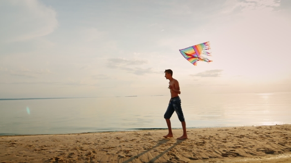 Teen Playing with a Kite Near the Sea in the Beautiful Colorfull Sky