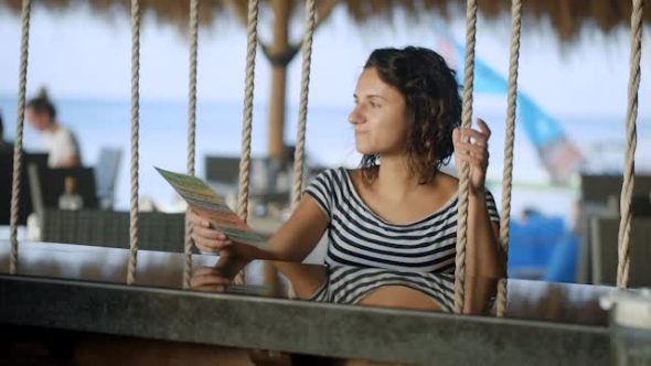 Brunette in a Striped Blouse with Bare Shoulders Sitting at the Bar and Rest. Excellent Weather