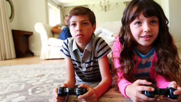 Siblings lying on rug and playing video game