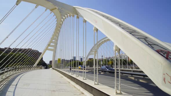 Walk through parallel leaning arch bridge with vehicles, sunny day