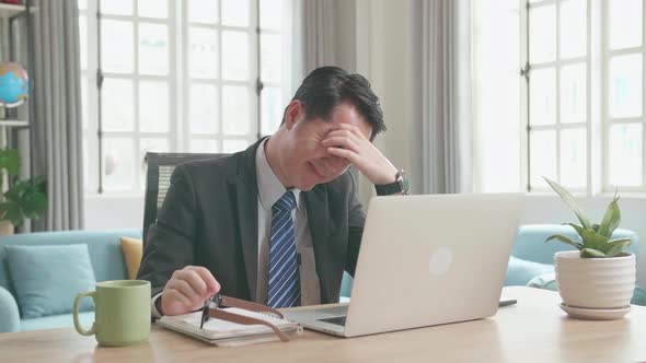 Tired Asian Businessman Taking Off The Glasses After While Using The Computer For Working At Home