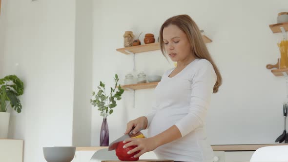 Pregnant Fairskinned Woman in the Kitchen Cuts Red Pepper