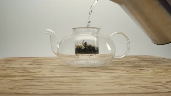 Pouring Boiling Water From Kettle Into White Tea in a Teapot on a Wooden Table