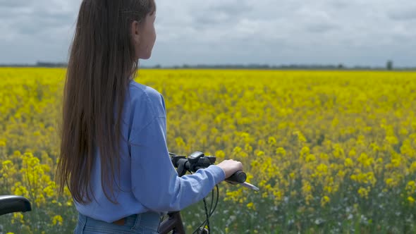 Teenager girl with a bicycle in a field of flowers.