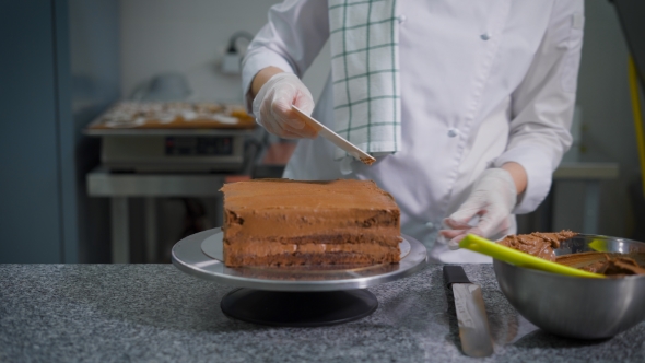 Confectioner with a Spatula Spread Chocolate on a Freshly Baked Cake on a Professional Kitchen in a