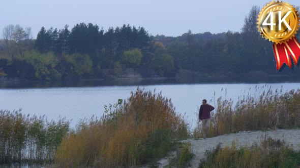 Man Stands For a While Near Lake River Sandy Bank