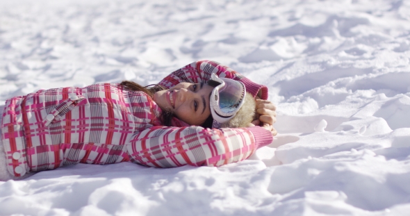 Young Woman Lying on Snow with Ski Goggles