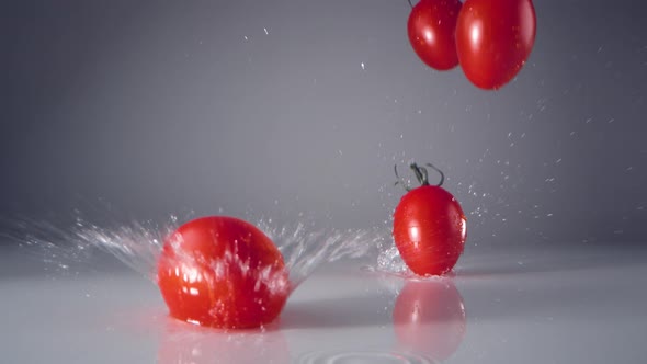 Fresh cherry tomatoes falling on water surface. Slow Motion.