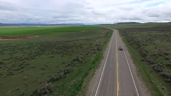 Drone flying past car slowly drive on road in vast landscape