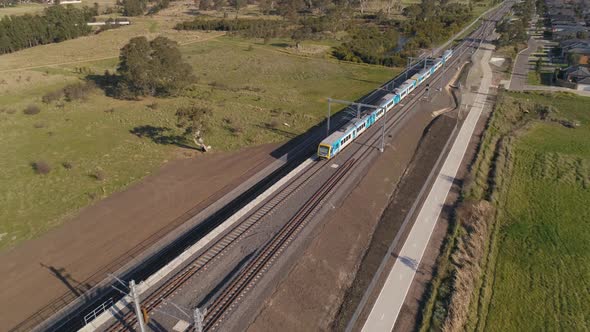 Train drives through outer suburbs aerial shot rising