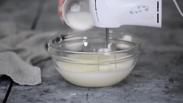 Female Hands Add a Sugar to the Bowl with Whipping Egg and Mix with Hand Mixer on Wooden Table