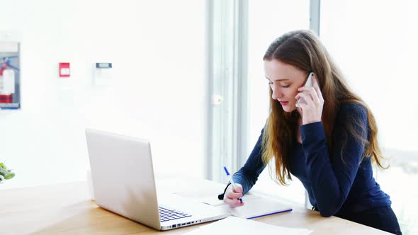 Business executive writing on diary while talking on mobile phone