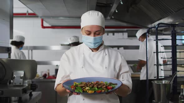 Portrait of caucasian female chef wearing face mask presenting dish