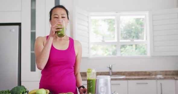 Relaxed asian woman drinking smoothie in kitchen