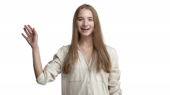 Video of Friendly Adult Woman with Braces and Necklace Wearing Beige Blouse Saying Hello and Waving