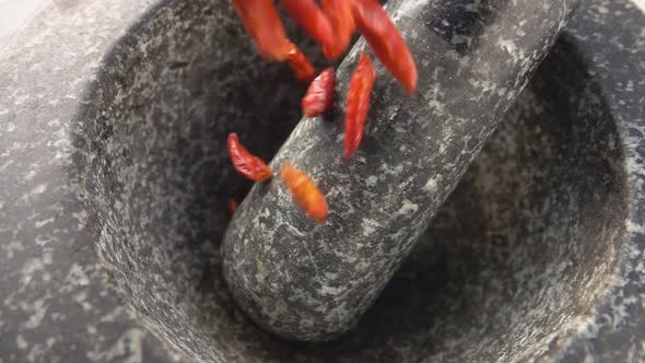 Close-up of Red Cayenne Pepper Pods Falling Into the Stone Mortar