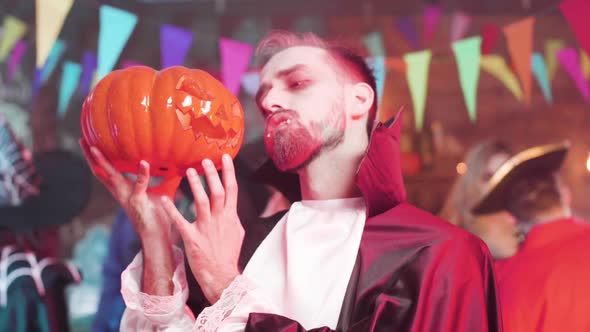 Man in Vampire Outfit Holds a Carved Pumpkin Head in His Hand