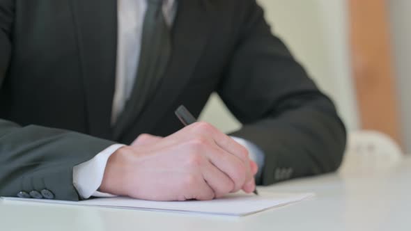 Close Up of Middle Aged Businessman Writing on Paper with Pen